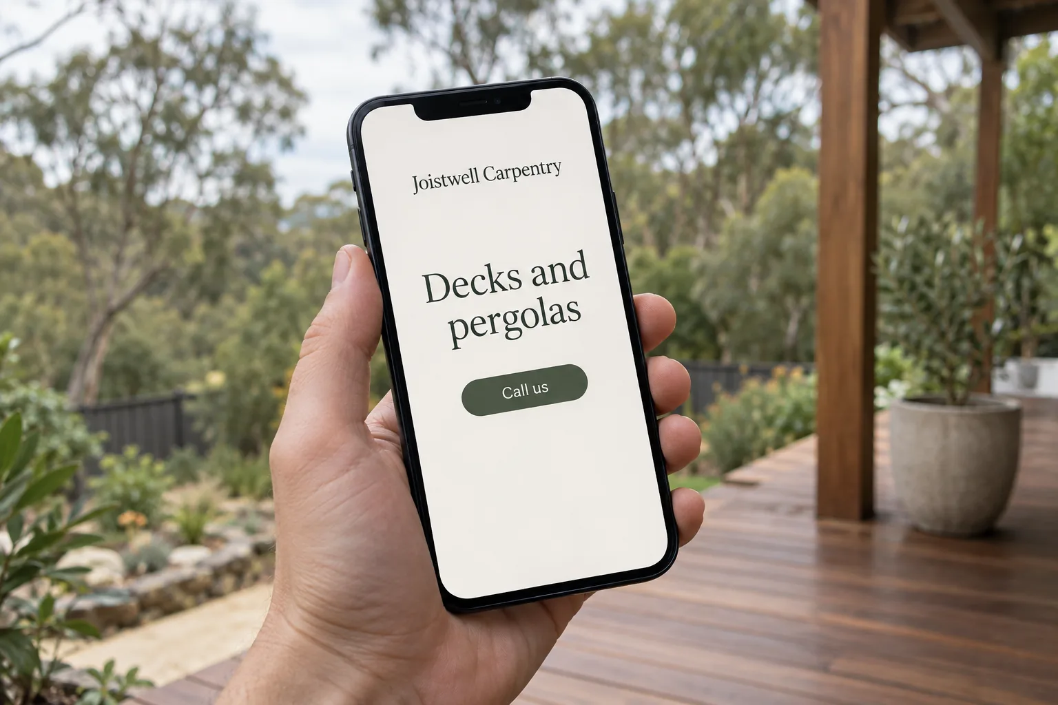A hand holding a phone showing a Joistwell Carpentry mobile website with a call button concept