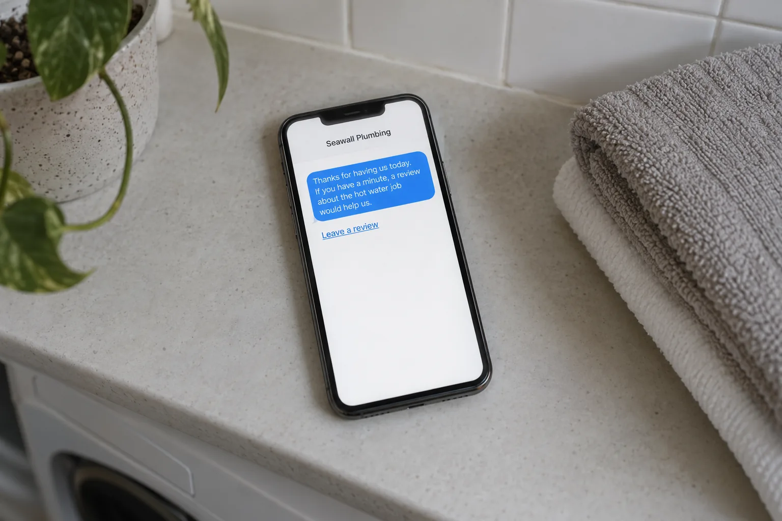 A phone on a laundry bench showing a Seawall Plumbing review request text message concept