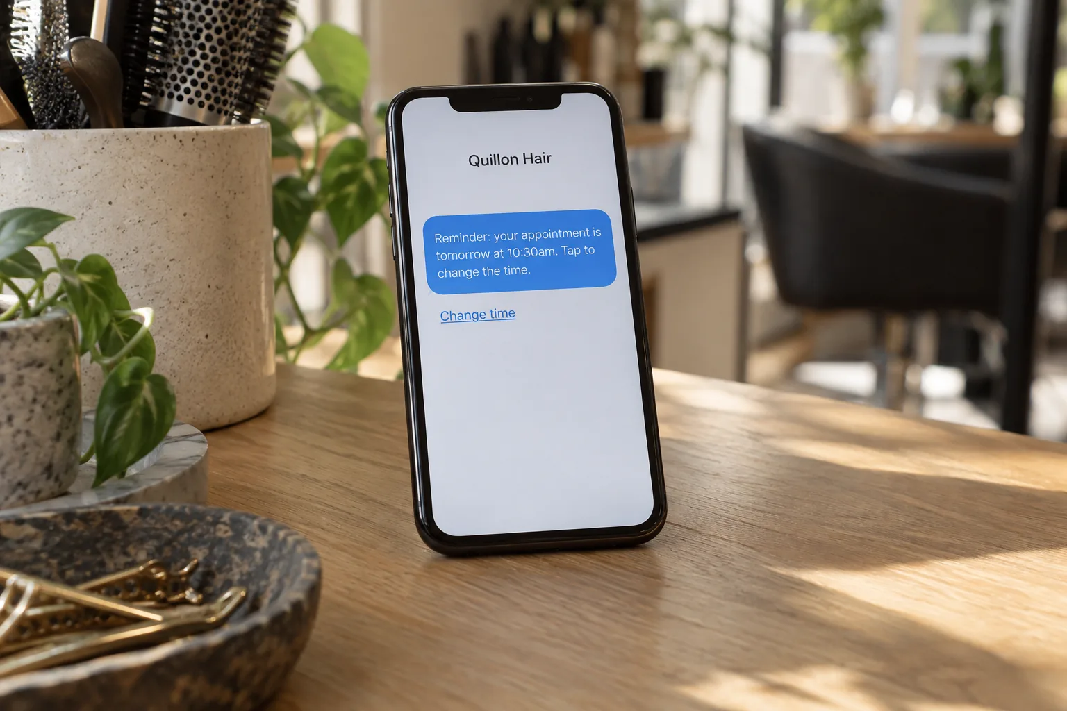 A phone on a salon counter showing a Quillon Hair appointment reminder text concept
