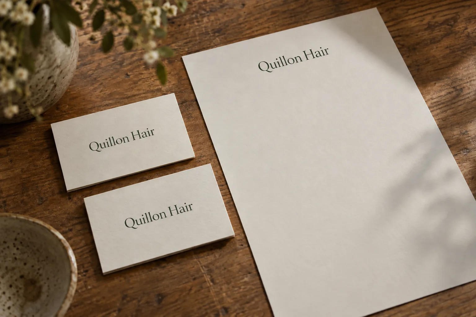 Printed business cards and a letterhead for Quillon Hair on a timber desk, a concept design
