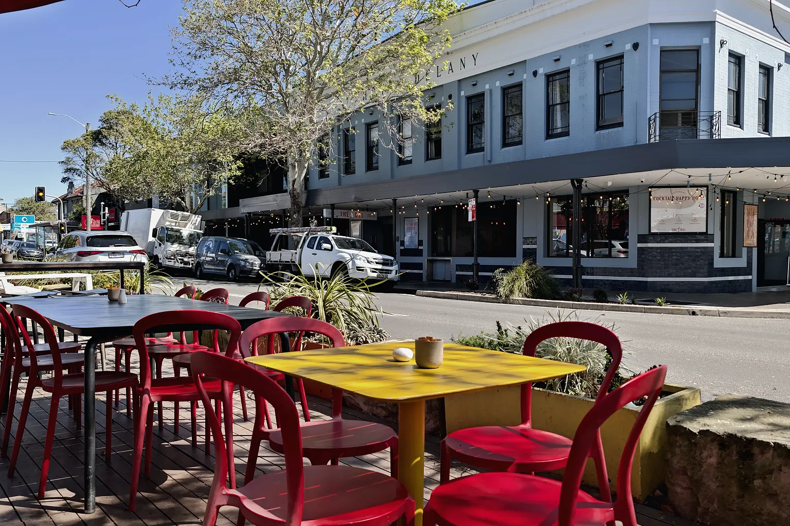 Red chairs and yellow tables outside a cafe on Darby Street, with a heritage corner building behind